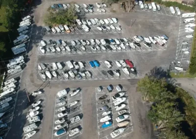 A parking lot filled with various boats, showcasing different sizes and colors, under bright sunlight.